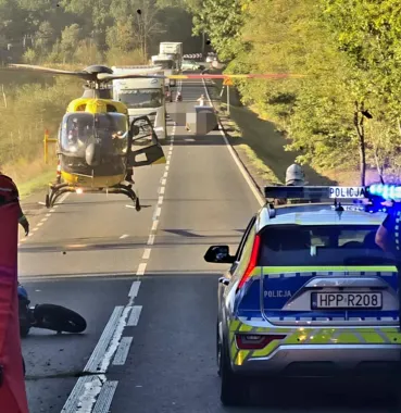 Śmigłowiec ratunkowy ląduje na zablokowanej drodze obok radiowozu policji podczas interwencji służb.