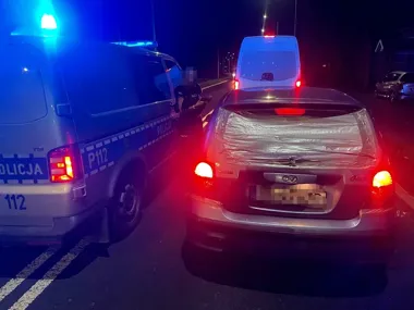 Policyjny radiowóz zatrzymał w nocy na drodze srebrne kombi z zabezpieczoną folią tylną szybą, obok stoi biały furgon.