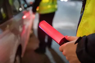 Funkcjonariusz w odblaskowej kamizelce trzyma czerwoną pałkę sygnalizacyjną podczas nocnej kontroli drogowej.